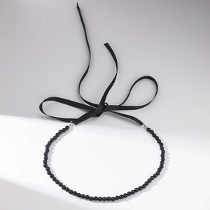 Detail of black crystal beaded floral necklace with long satin silk ribbons on grey background