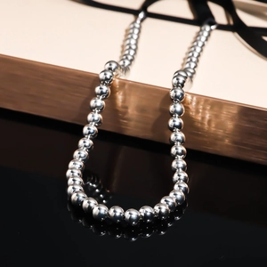 Detail of silver beaded necklace showing polished metallic beads on reflective black surface