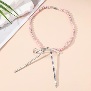 Vue détaillée du collier en perles de marbre rose avec un grand pendentif nœud en métal argenté