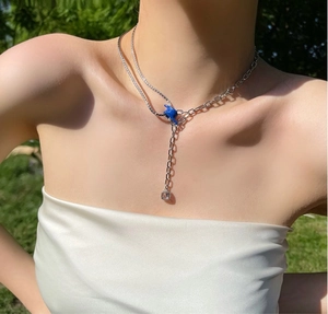 Detail of silver layered necklace with blue enamel hand charm and square zircon pendant