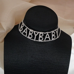 Gros plan du collier choker BABYBABY en strass étincelants sur un support de bijoux noir