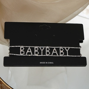 Gros plan du ras-du-cou argenté avec lettres BABYBABY en strass sur tissu de soie