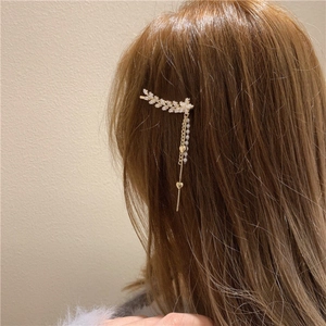 Détail d'une pince à cheveux feuille dorée avec strass et pompons perlés sur cheveux