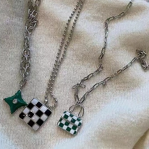 Tres collares estilo hip-hop con colgantes de damero y estrella sobre punto crema
