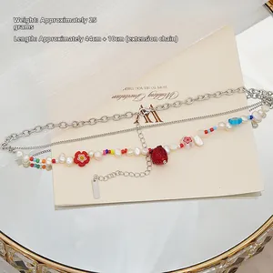 Vue détaillée du collier multicouche avec breloques fraises, perles et dimensions de longueur