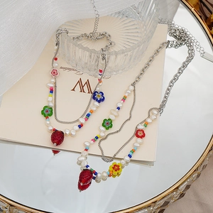 Détail d'un collier de perles avec fraise en verre et fleurs sur un plateau miroir