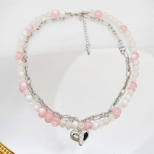 Détail d'un collier double épaisseur avec pendentif cœur argenté et perles œil de chat roses