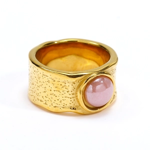 Close-up of gold irregular hammered texture wide band ring with pink ceramic stone inlay