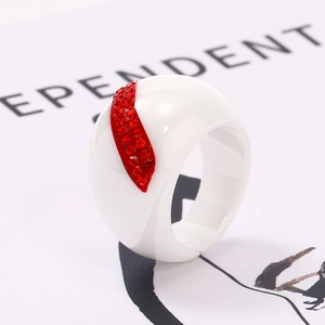 Macro shot of wide white ceramic ring with red crystal leaf pattern on magazine page