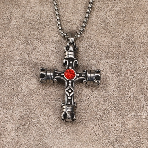 Macro detail of gothic silver cross pendant with a red gemstone on stone background