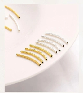 Detailed view of 14K gold and silver curved tube beads with twisted and matte textures