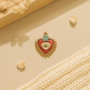 Detail of red heart Evil Eye pendant with gold plating on soft fabric and dried flowers