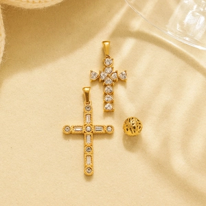 Golden cross pendants with cubic zirconia and filigree bead on beige textured background