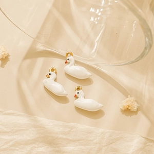 Trois pendentifs cygnes blancs pour porte-clés DIY avec attaches dorées sur fond beige mat