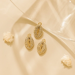 Close-up of gold-plated 18K shell pendants with sparkling crystals on beige fabric