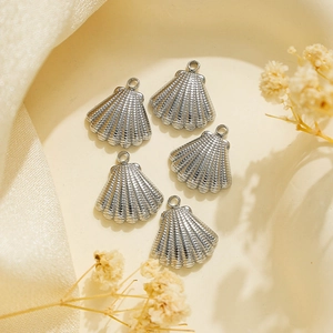 Gros plan de cinq pendentifs coquillages argentés pour bijoux DIY sur un plat beige