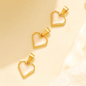 Detailed macro view of heart-shaped gold pendants with white inlay and milgrain edges