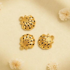 Detalle de tres dijes de concha dorados con puntos negros para creación de joyas DIY
