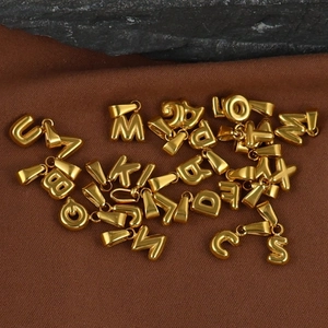 Macro shot of 18K gold plated stainless steel bubble letter charms on brown fabric
