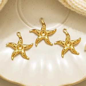 Three 18K gold plated starfish charms for DIY jewelry making in a beige shell dish