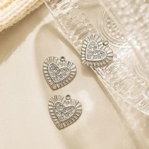 Detalle de tres colgantes de corazón plateados con strass y borde texturizado para joyas DIY