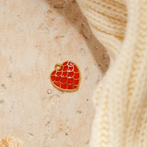 Macro detail of red enamel heart charm with golden fish scale pattern and metal loop