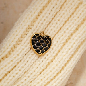 Macro shot of heart-shaped gold pendant with black enamel fish scale pattern on knit fabric