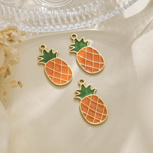 Macro detail of three handmade pineapple charms with vibrant orange and green enamel finish