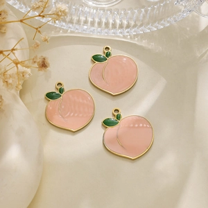 Detailed view of pink enamel peach charms with gold edges and green leaves on a tray