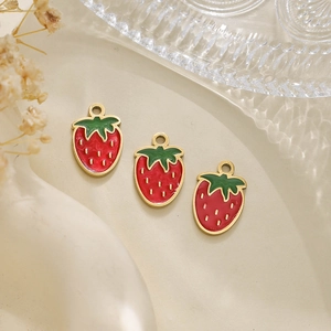 Detailed close-up of three strawberry pendants with red and green enamel on gold finish