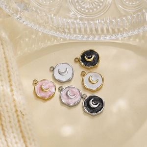 Gros plan de six pendentifs lune en acier inoxydable avec émail coloré sur tissu beige