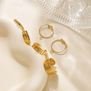 Nahaufnahme goldener DIY Schmuck-Komponenten und Ringe auf weichem Stoffhintergrund