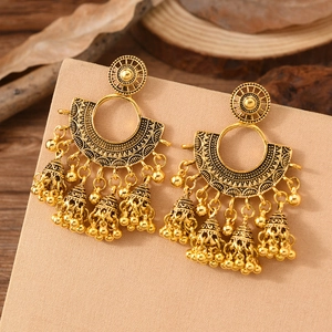 Detail of bohemian gold-finish tassel earrings with filigree pattern and metal bells