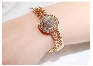Detail van een roségouden kettingarmband met een glinsterende ronde schijf met diamanten