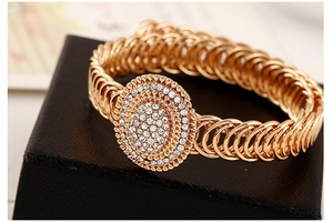 Detail van een geschakelde goudkleurige armband met een sprankelende hanger met strass