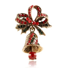 Détails d'une broche cloche de Noël avec strass rouges et un nœud en alliage doré
