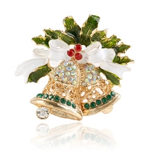 Détail d'une broche cloche de Noël avec feuilles de houx et baies rouges en alliage doré