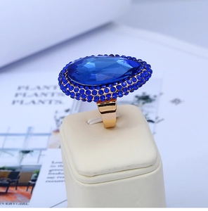 Macro shot of large oval blue crystal ring with gold plating on a leather display stand