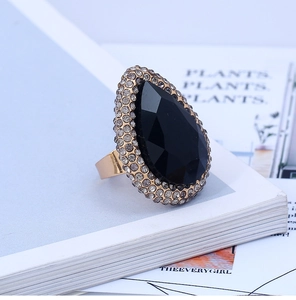 Detail of a large pear-shaped black stone statement ring with crystal halo on gold band