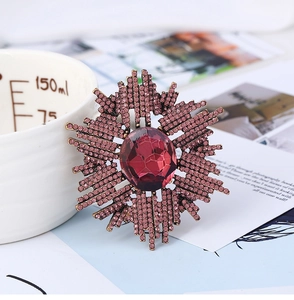 Détail d'une broche soleil vintage avec pierre rouge et cristaux violets sur base dorée
