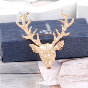 Close-up of golden alloy deer head brooch showing detailed texture and antlers on dark blue box