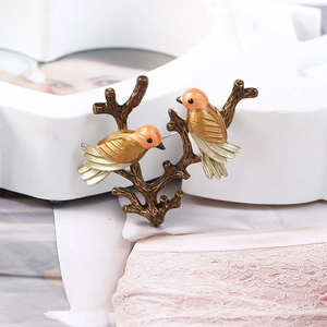 Close-up of bird brooches with orange enamel feathers on a metallic branch detail
