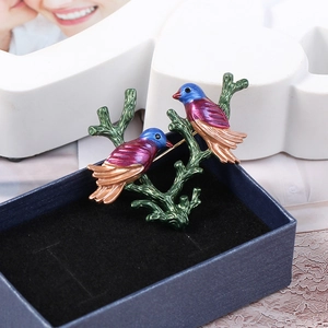 Close-up of a colorful enamel double bird brooch on a branch with gold and blue details