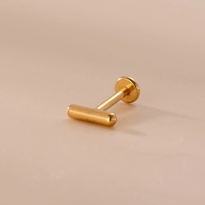 Dettaglio di un labret dorato da 16G con design a barra a T minimalista per piercing al labbro