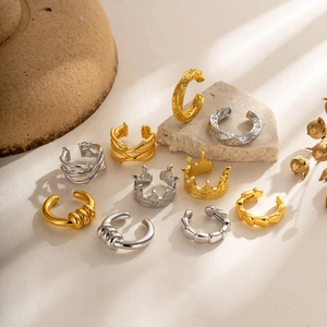 Set of minimalist C-shaped gold and silver ear cuffs on stone background