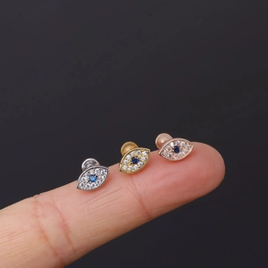 Macro shot of micro-pave evil eye ear studs in silver, gold, and rose gold on a fingertip