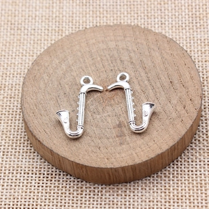 Pair of saxophone shaped metal pendants for DIY jewelry making on a wooden base