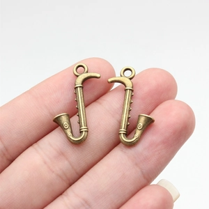 Pair of vintage bronze saxophone charms for jewelry making, held to show small scale