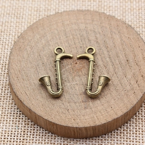 Pair of vintage bronze saxophone charms on rustic wood and woven fabric base