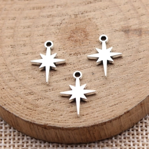 Three silver starburst North Star charms on a wood block for DIY jewelry making